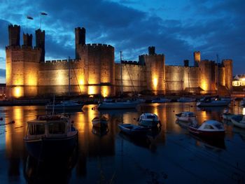 Boats moored in river against illuminated buildings in city