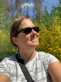 Portrait of woman wearing sunglasses against trees, enjoying the beautiful sun, mobile phone selfie