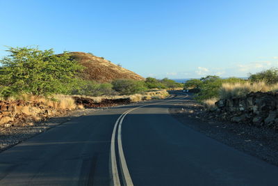 Road amidst trees against clear blue sky