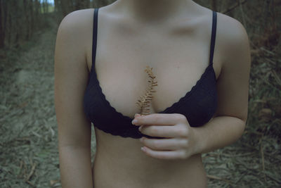 Midsection of woman wearing bra while holding leaf outdoors