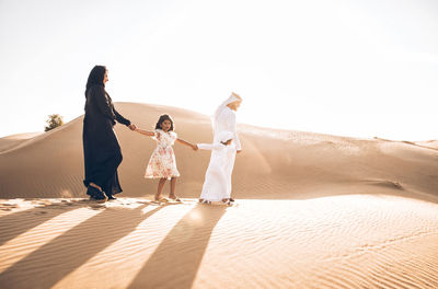 Arabian family standing at desert against sky