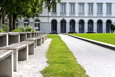 Benches and tables with flowers arranged in a row in the park, in the background a large building.