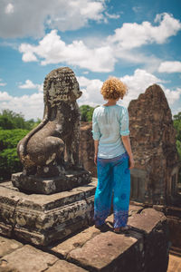 Woman standing by old statue at temple against sky