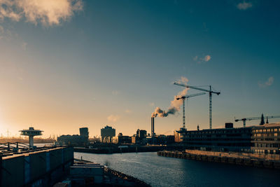 City by river against sky during sunset