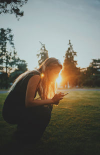 Woman using mobile phone on field against sky during sunset