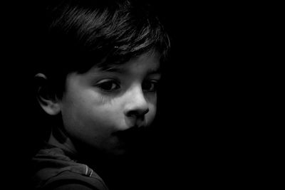 Close-up portrait of cute boy against black background