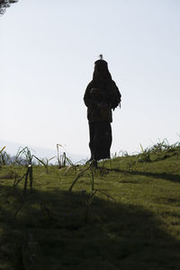 Rear view of man walking on field against clear sky