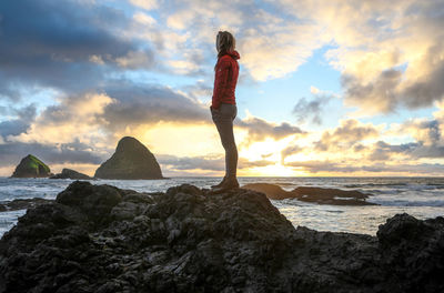 Rear view of woman standing on rock by sea against sky