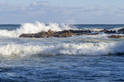 Waves splashing on shore against sky