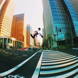 Full length of man jumping on street against modern buildings in city