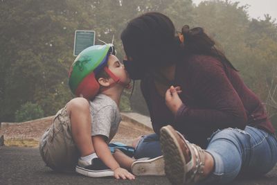 Mother wearing mask kissing son sitting on road