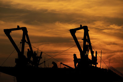 Silhouette cranes at construction site against sky during sunset