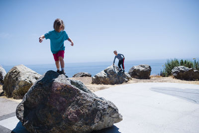 Siblings playing on rocks against sea and sky during sunny day