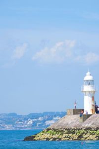 Lighthouse by sea against blue sky