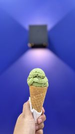 Cropped hand holding ice cream cone against blue background