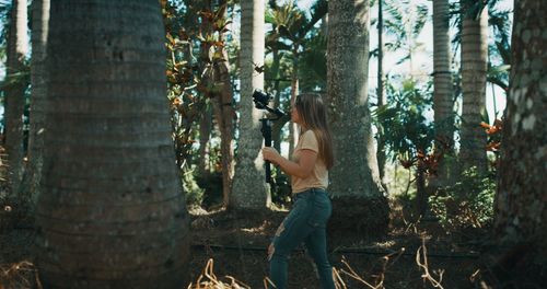 Side view of woman standing by tree trunk in forest