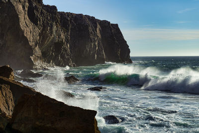 Sea waves splashing on rocks against sky