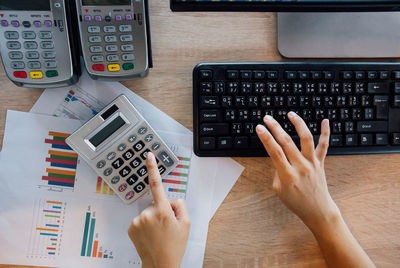 Cropped image of woman using calculator and computer at office