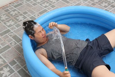 High angle view of smiling woman holding garden hose while lying on inflatable pool