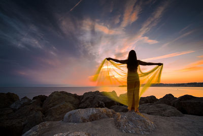 Woman in a yellow dress and cape observing a magnificent sunrise on the french basque coast iv