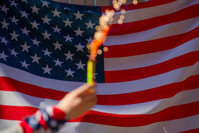 Cropped hand holding sparkler against american flag