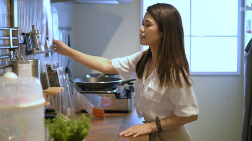 Side view of a young woman standing in kitchen