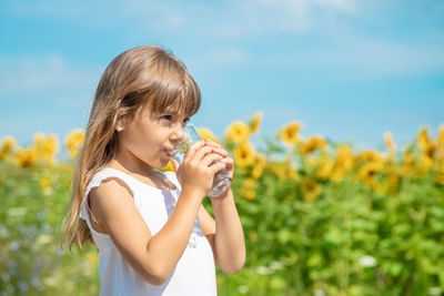 Young woman drinking water while standing against plants