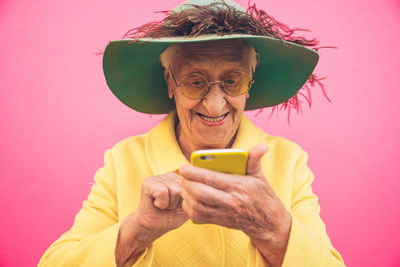 Close-up of smiling senior woman using phone against pink background