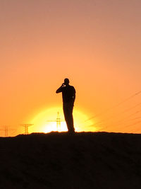 Silhouette man standing on landscape against orange sky