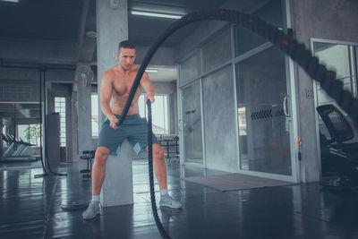 Full length of shirtless man exercising in gym