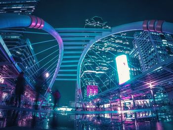 Wet walkway amidst modern illuminated buildings in city