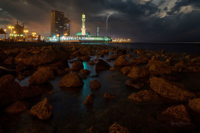 Illuminated rocks by sea against sky at night