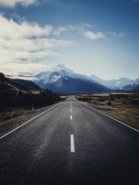 Empty road leading towards mountains against sky