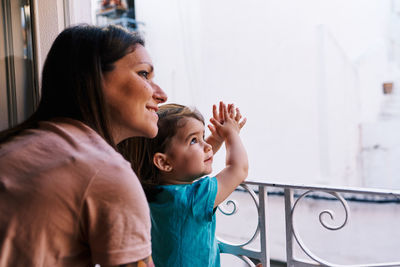 Mother and daughter looking out the window of the house happy