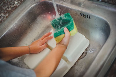 Cropped hands washing container in kitchen sink