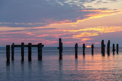 Wooden posts in sea against sky during sunset