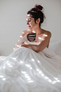 Woman sitting on bed while holding coffee cup at home