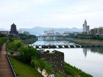 View of buildings by river in city against sky