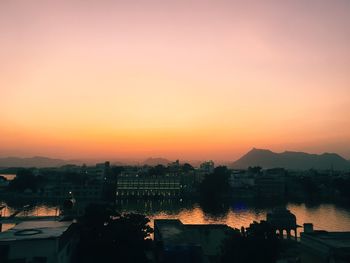 Silhouette city by sea against orange sky