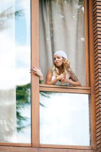 Low angle view of woman leaning on window frame