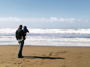 Rear view of father standing with baby at beach on sunny day