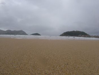 View of calm beach against cloudy sky