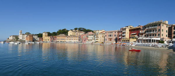 Sailboats in canal by buildings against clear blue sky