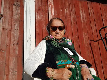 Portrait of woman wearing sunglasses against wooden wall