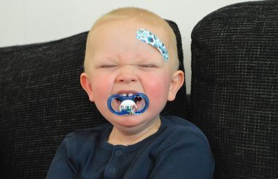 Close-up cute boy with pacifier in mouth crying at home