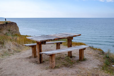 Wooden bench on shore by sea against sky