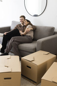 Happy couple embracing while sitting on sofa by cardboard boxes at home