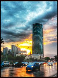 Cars on city street against cloudy sky at sunset