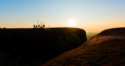 Silhouette rocks on land against sky during sunset