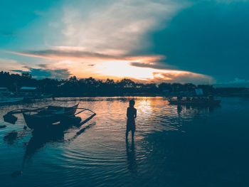 Silhouette boy standing on beach against sky during sunset